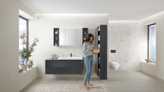 Woman opens tall cabinet with lots of storage space in bathroom with Geberit Acanto bathroom furniture Woman opens tall cabinet with lots of storage space in bathroom with Geberit Acanto bathroom furniture