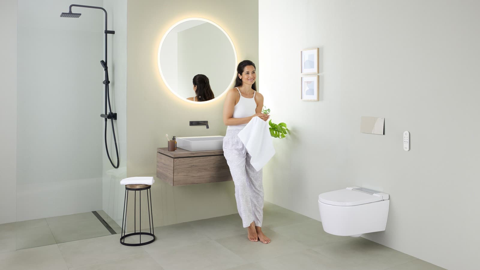 Woman leaning on a washbasin in a bathroom with Geberit AquaClean Sela shower toilet and Geberit VariForm washbasin and furniture Woman leaning on a washbasin in a bathroom with Geberit AquaClean Sela shower toilet and Geberit VariForm washbasin and furniture