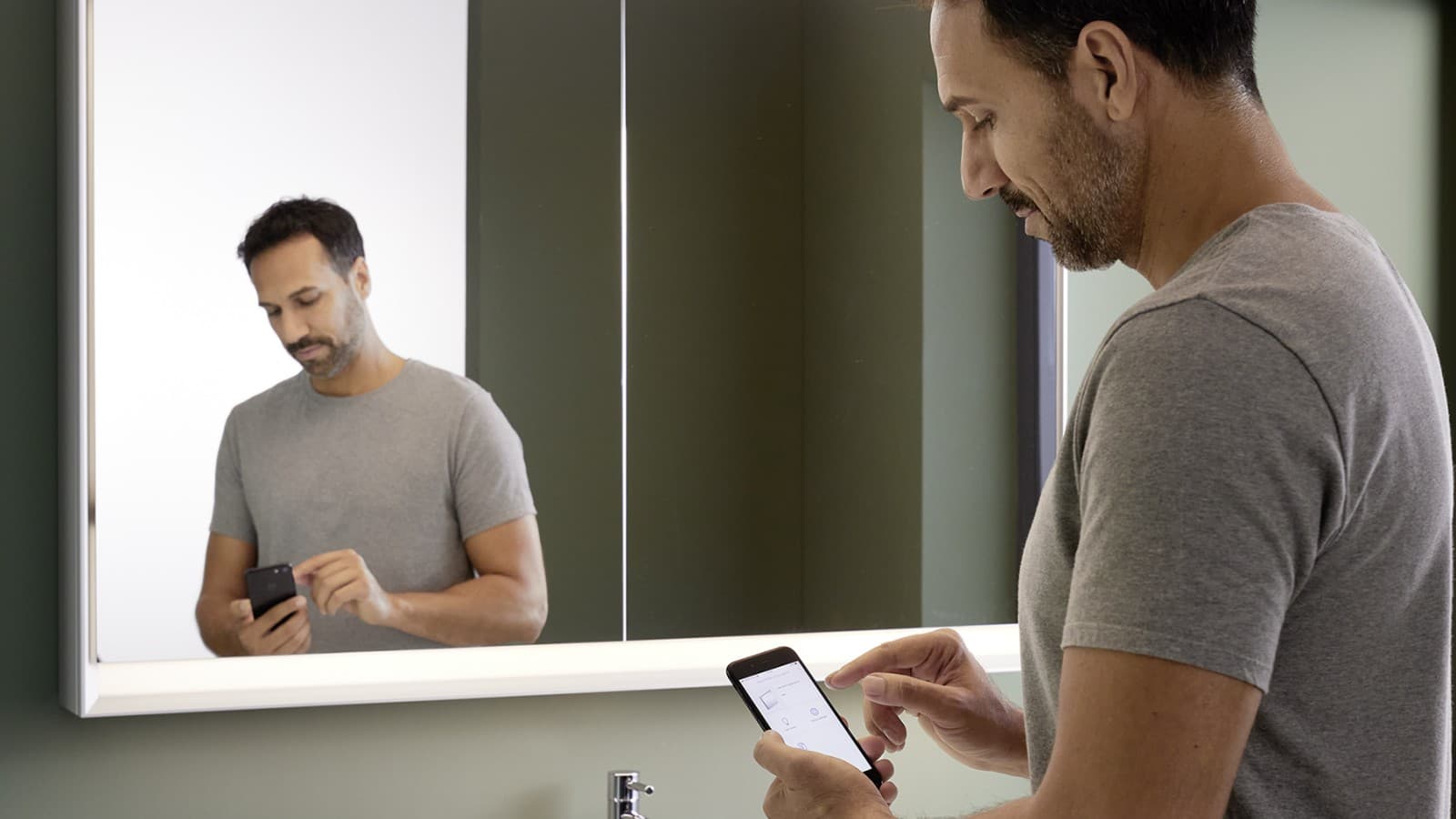 Man controlling a mirror with Geberit ComfortLight lighting using his mobile phone Man controlling a mirror with Geberit ComfortLight lighting using his mobile phone